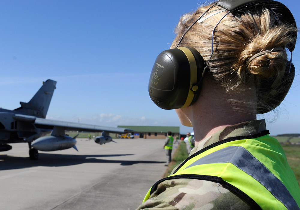 A female Royal Air Force groundcrew member is looking at a plane on the runway
