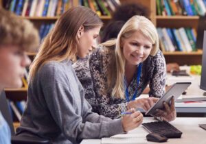 A teacher is working with her students with computers and tablet devices