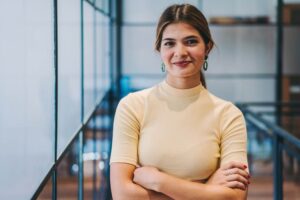 A young international business woman stands arms folded smiling