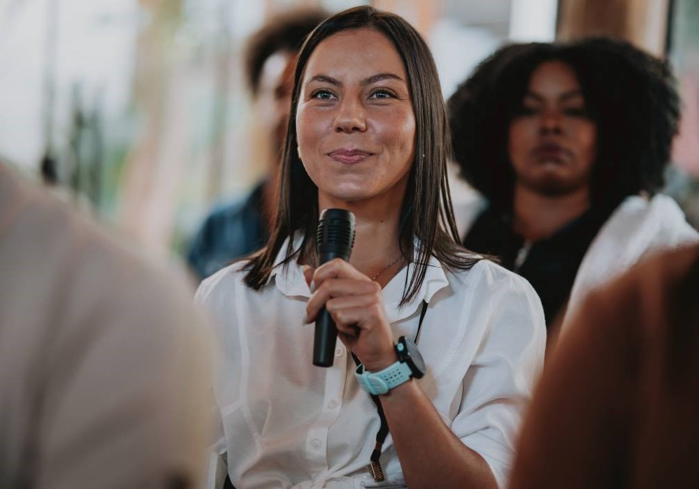 A public health practitioner sits in an audience with a microphone