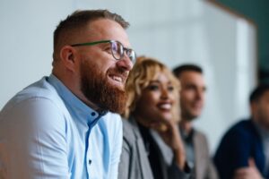 man smiling as he listens in during meeting with colleagues sitting to side of him - jobs with mba blog